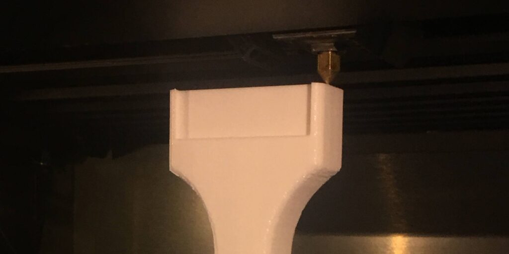 3D printing process of a white PVC beer tap handle in a dimly lit setting.