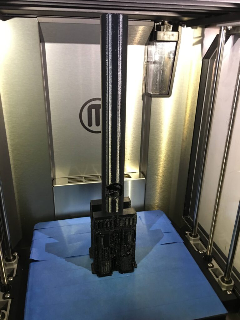 M logo 3D printer creating a detailed beer handle model in a clear enclosure.