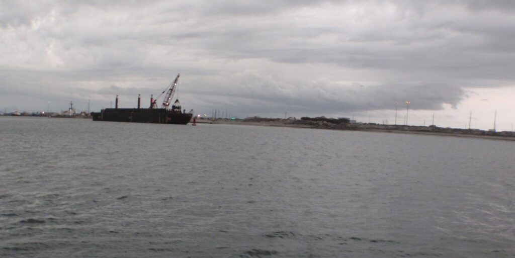 Industrial cargo ship anchored near coastal facilities under overcast sky.