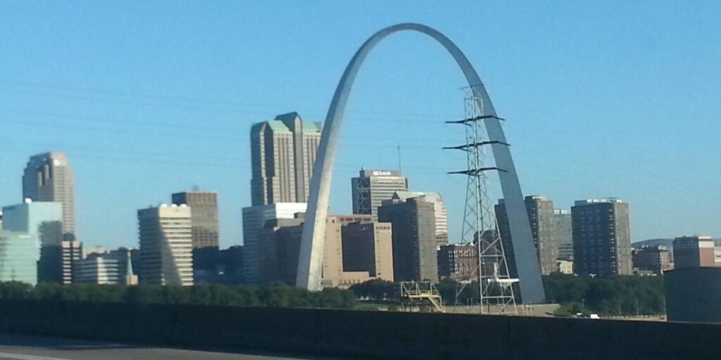 Iconic Gateway Arch towering over diverse St. Louis skyline in sunny weather.