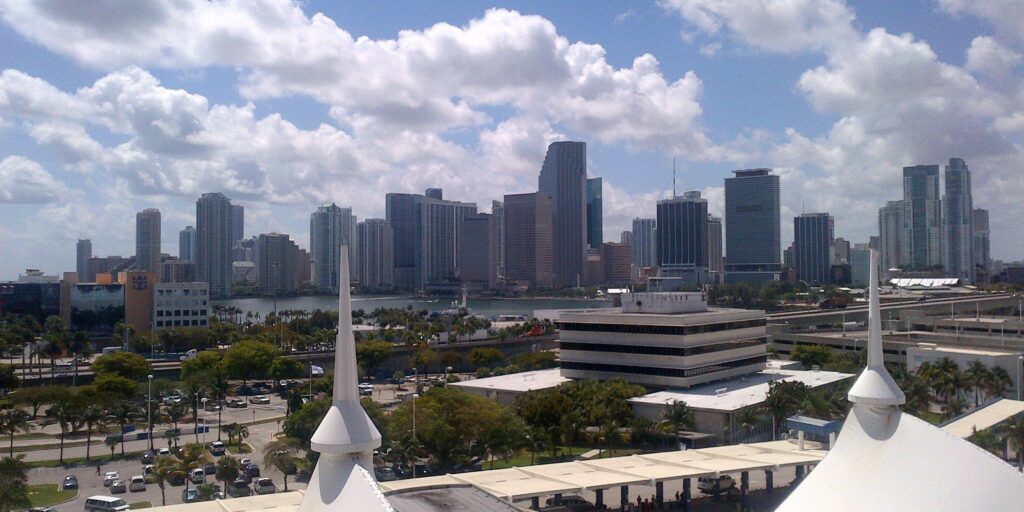 Miamis sunny skyline featuring modern high-rises and classic spires under a blue, partly cloudy sky.