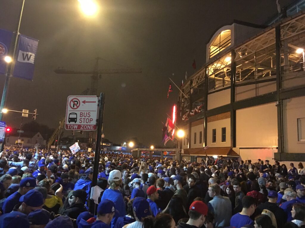 Excited Chicago Cubs fans celebrating a nighttime World Series victory outside the stadium.