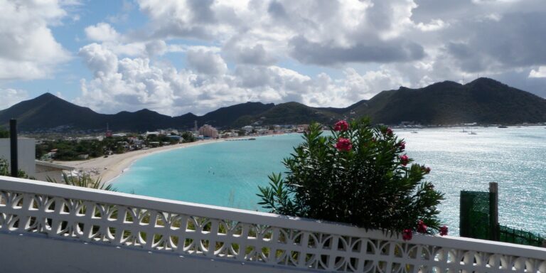 Sint Maarten balcony view showcasing turquoise sea, lush hills, and vibrant flowers.
