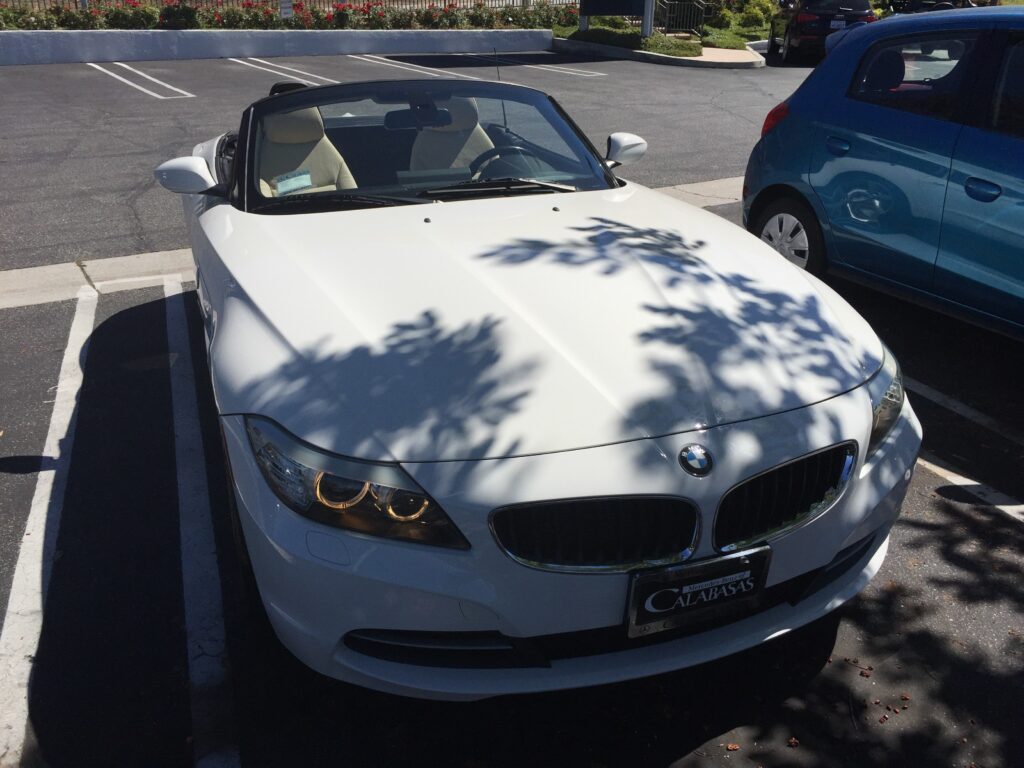 White BMW Z4 parked askew in sunny California lot with tree shadow on hood.